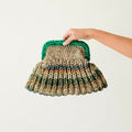 Hand holding a woven clutch bag with a green handle on a light background