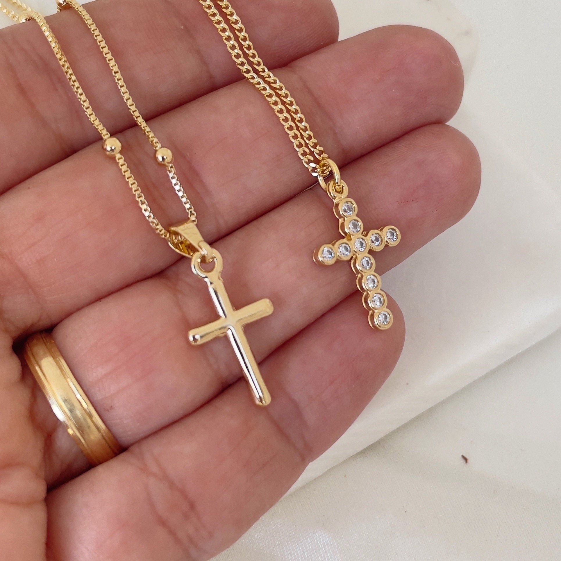 Cross Necklace, plain cross pendant and crystal cross pendant. Materials: 18k gold filled and cubic zirconia, shown in hand and white silk background