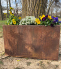 A large rectangular metal trough planter with various flowers planted in it, placed outdoors.