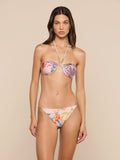 A woman wears the Suki Halter Bikini Top with matching bottoms, standing against a plain beige background and gazing at the camera with a neutral expression.