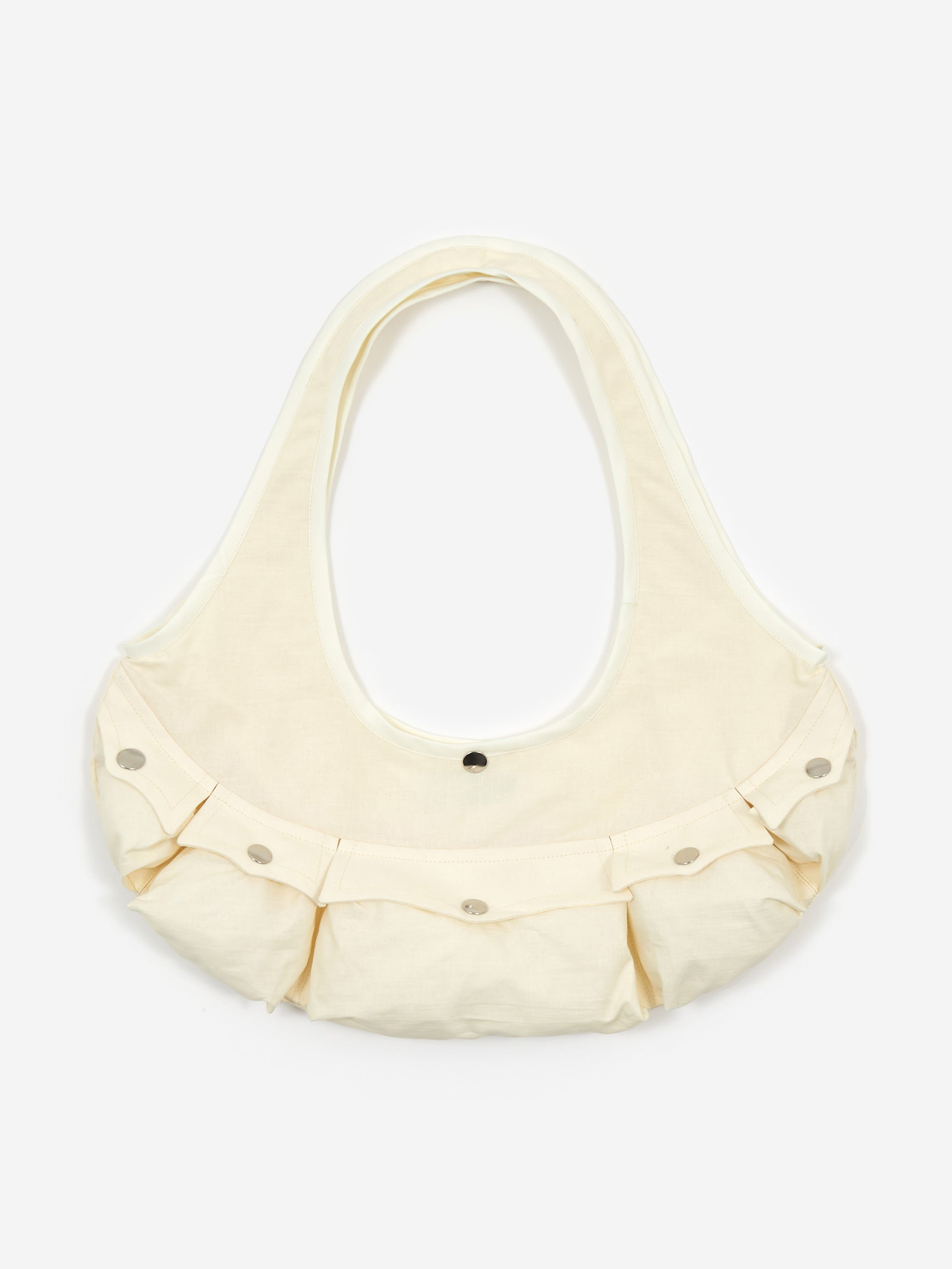 The Sam Pomeroy Cargo Handbag - Cream by Sam Pomeroy is a cream-colored, crescent-shaped handmade handbag featuring three front pockets with silver snap buttons. It boasts a wide strap and minimalist design, displayed against a plain white background.