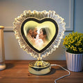 Heart-shaped photo lamp displaying a couple kissing on a wooden surface with a plant in the background.