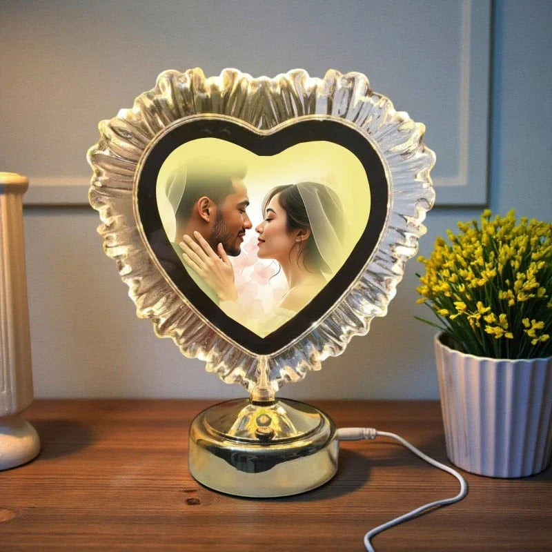 Heart-shaped photo lamp displaying a couple kissing on a wooden surface with a plant in the background.